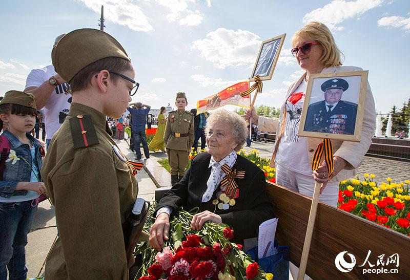 一名身着二战苏式军服的儿童向老兵送上鲜花和节日的祝福（人民网记者 屈海齐 摄）